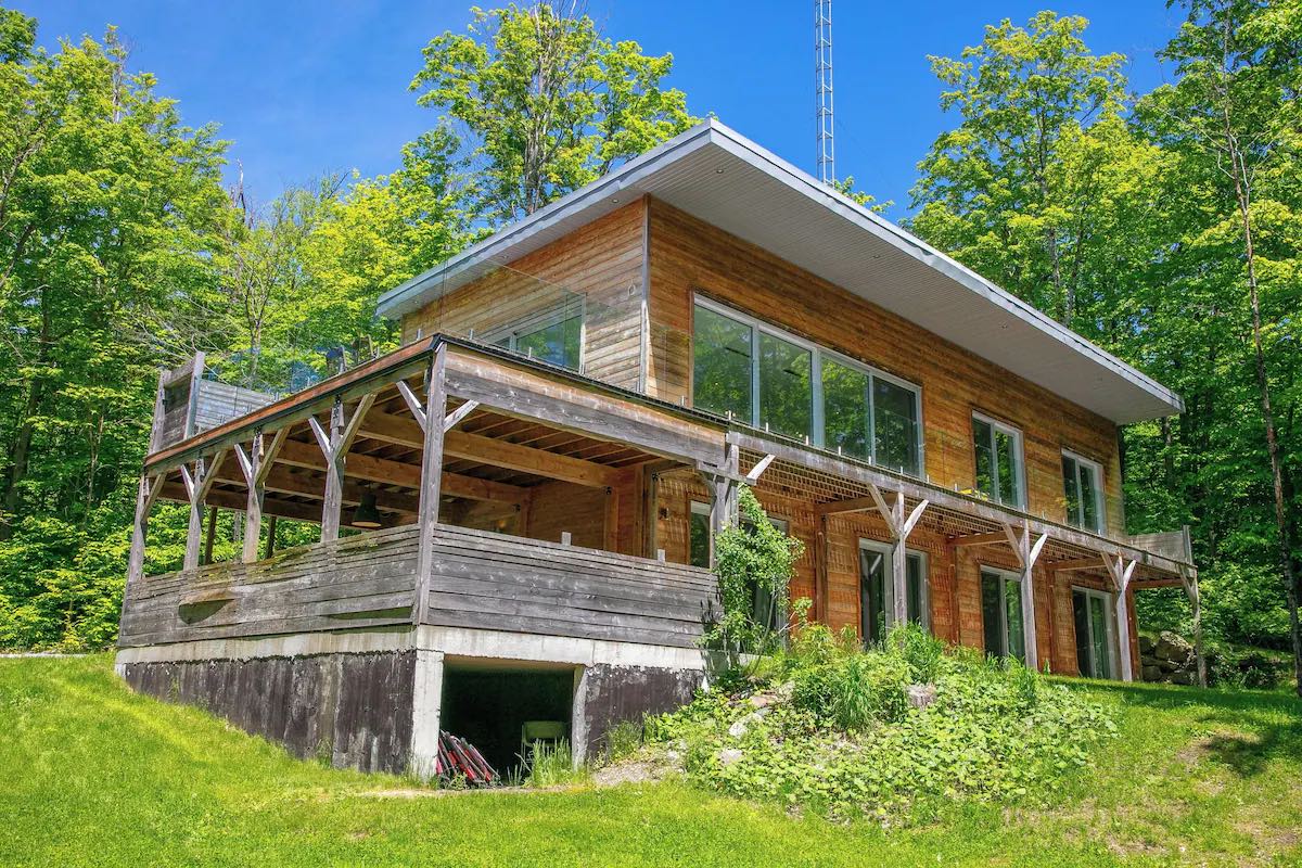 Le chalet, en bois, avec sa grande terrasse couverte et la forêt derrière